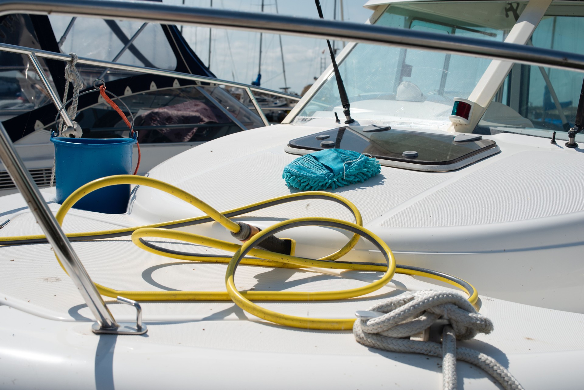 Boat cleaning equipment. Plastic bucket, hose with water spray gun, mop laying on the yacht.